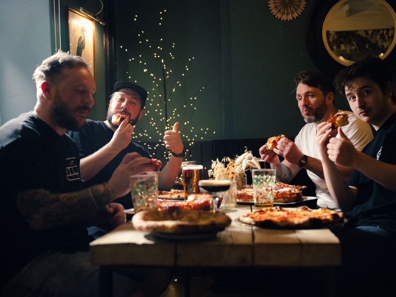 Friends sharing Detroit and New York pizzas and pints at a table inside The Towpath Inn