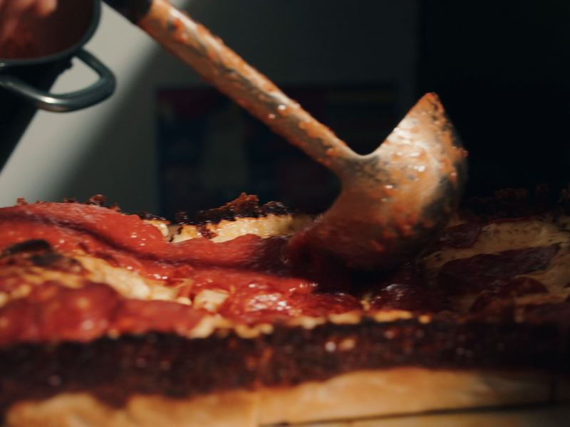 Sauce ladled in stripes over a Detroit pizza with a dark caramelised cheese edge